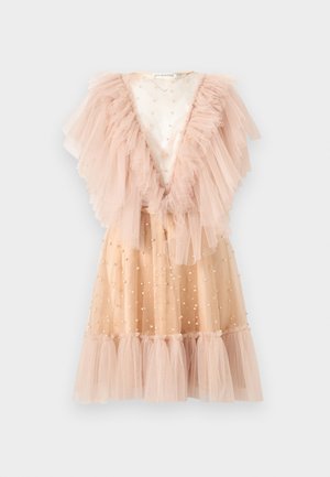 Femme debout portant une robe en tulle couleur pêche avec des volants et des détails en perles, associée à des sandales à talons hauts nude à brides à la cheville sur fond blanc.