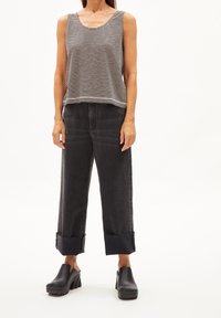 Donna che indossa una canotta a righe bianche e nere, jeans neri ampi con risvolti e zoccoli neri con plateau, in piedi davanti a uno sfondo semplice.