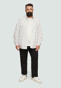 Weißes Hemd mit bunten Punkten, über einem weißen T-Shirt, kombiniert mit schwarzen Nadelstreifen-Hosen und weißen Turnschuhen. Lässiger Stil.
