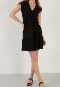 Svart kort klänning med djup V-ringning, korta ärmar, knytmidja och lager-på-lager kjol. Tillverkad av strukturerad tyg med en avslappnad passform.