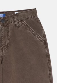 Pantaloni casual marroni con tasca frontale diagonale, passante per cintura e cuciture visibili su sfondo bianco.