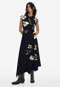 Schwarzes Blumenmaxikleid mit kurzen Ärmeln, das große rosa und grüne Blumen zeigt. Glattes Material mit asymmetrischem Saum, kombiniert mit schwarzen Cowboy-Stiefeln.