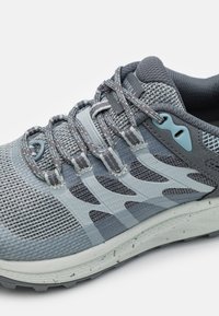 Scarpa atletica da uomo con tomaia in mesh nei toni di grigio, superficie texturizzata, lacci piatti e suola in gomma grigia chiara con accenti maculati.