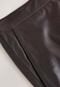 Ciemnobrązowa skóra o gładkiej fakturze; cechuje się subtelnymi zmarszczkami i prostym wzorem z czystym przeszyciem wzdłuż krawędzi.