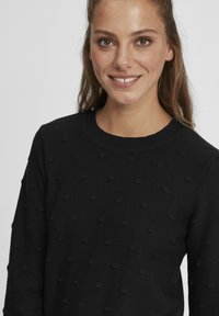 Pulover negru cu model texturat de bobble, guler rotund și mâneci lungi. Fabricat din material tricotat, având o textură moale și netedă.