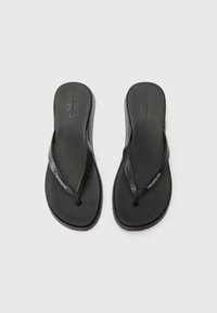 Sorte flip-flops med en teksturert gummisåle og glatte stropper med logo. Rund form med minimale designelementer.