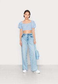 Top cropped em padrão xadrez azul com mangas bufantes, combinado com jeans de cintura alta em tom claro. Completo com tênis brancos e uma bolsa azul.