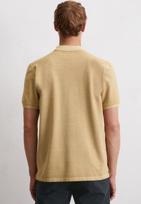 Koszula polo z krótkim rękawem w jasnym odcieniu beżu, z kołnierzykiem, prostym krojem oraz miękkim, teksturowanym materiałem o schludnym wykończeniu.