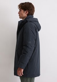 Dunkelblaue Parka-Jacke mit Kapuze, ausgestattet mit einem Reißverschluss, Seitentaschen und einer aufgesetzten Tasche am Ärmel. Glatte äußere Textur.