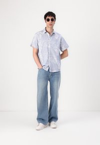 Camicia floreale azzurro chiaro a maniche corte, taglio rilassato, abbinata a jeans blu larghi e sneakers bianche, occhiali da sole completano il look.
