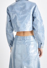 Beskarvad ljusblå jeansjacka med paljetter, långa ärmar, krage och guldknappade manschetter, ihopparad med en matchande paljettfodrad högmidjad kjol.