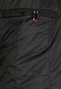 Schwarze Pufferjacke aus Material mit einer glatten, leicht glänzenden Textur. Verfügt über einen Knopfverschluss mit roten, weißen und blauen gestreiften Akzenten am Hals.