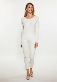 Tricou alb cu mâneci lungi și decolteu rotund, asortat cu pantaloni albi strâmți și pantofi plate bej deschis, cu un detaliu sub formă de fundiță.