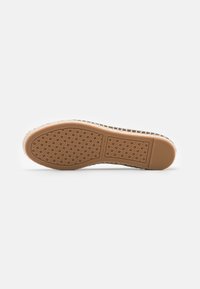 Chaussure à semelle en caoutchouc avec une surface texturée, de couleur marron et à motif à pois, ornée du nom de la marque "Tory Burch."