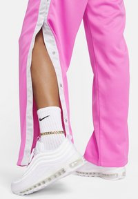 Rozā sporta bikses ar baltām pogām, ar sānu izgriezumu. Kombinētas ar baltām Nike Air Max kedām un strukturētām baltām zeķēm.