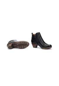 Botas de cuero negro hasta el tobillo con cremallera lateral y tacón medio apilado, una bota en posición vertical y la otra mostrando la suela de goma con patrón.