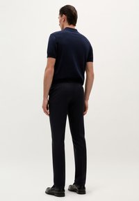 Polo de marina con mangas cortas, combinado con pantalones oscuros y zapatos negros; textura suave y ajuste entallado. Modelo de espaldas a la cámara.