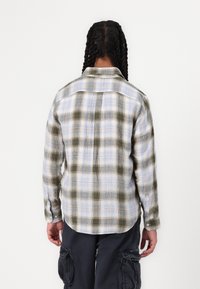 Camisa de botones con patrón de cuadros en tonos de azul, verde y crema. Manga larga, corte relajado y detalle en el yugo de la espalda.