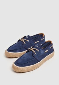 Zapatos de barco de ante azul marino con suela de yute trenzada. Presenta acentos en color beige, cordones decorativos y un forro interior estampado.