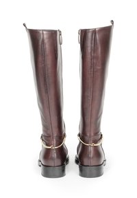 Brązowe, skórzane, sięgające do kolan botki o gładkiej fakturze, z zamkami błyskawicznymi po bokach oraz złotymi dodatkami na kostce. Solidne czarne gumowe podeszwy.