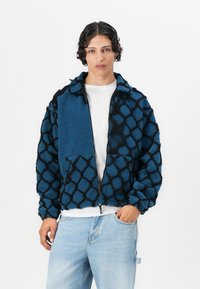 Blue fuzzy jacket featuring a black geometric pattern, zip closure, and side pockets; textured fabric; casual design with a slight crop.