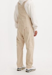 Peto de pana beige con rayas verticales, con bolsillos laterales, ajuste relajado y una sudadera con capucha beige a juego debajo.