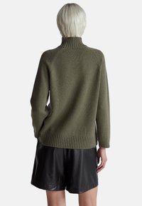 Olivově zelený pletený svetr s vysokým límcem, žebrovaným lemem a dlouhými rukávy, v kombinaci s černými koženými šortkami. Texturovaná látka s volným střihem.