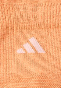 Oranžist kootud kangas, millel on suurepärane valge Adidas logo. Tekstuur on sile ja nähtavad õmblusmustrid.