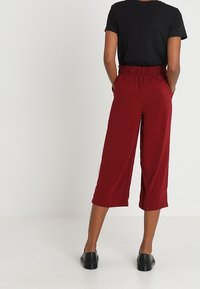 Röda, korta byxor med elastisk midja och lös passform, kombinerade med en svart T-shirt. Slät tyg och ankellång design.
