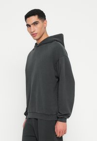 Dunkelgrauer Kapuzenpullover aus weichem Stoff, mit lockerer Passform, langen Ärmeln und einer Kängurutasche. Schlichtes Design mit gerippten Bündchen.