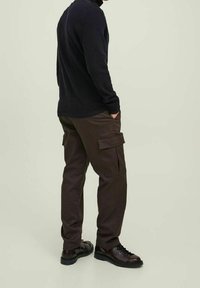 Bruine cargobroek met zijzakken, gemaakt van duurzaam materiaal. Gecombineerd met een donker langarmshirt en zwarte veterschoenen.