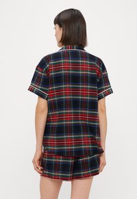 Short-sleeve pajamas in a red, green, and blue plaid pattern. Made of soft fabric, featuring a collared neck and relaxed fit shorts.