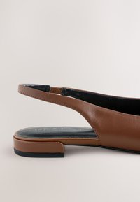 Chaussure plate slingback en cuir marron avec semelle intérieure noire et petit talon bloc sur un fond neutre.