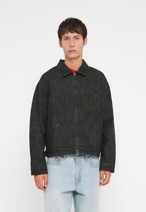 Black and white striped jacket with a collar, front zipper, and chest pocket; features two side pockets and a cropped design.