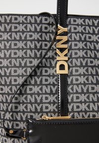Borsa a rete bianco e nero con logo ripetuto "DKNY", dettagli lucidi neri e charm con logo in tonalità oro. Include una tasca con zip.