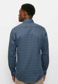 Marineblaue Hemdjacke mit einem geometrischen Muster in Blau, Weiß und Rot. Lange Ärmel und Standardkragen, taillierte Passform, Baumwollmaterial.