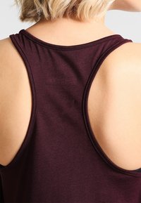 Débardeur bordeaux à dos nageur. Fabriqué en tissu doux, avec une texture lisse et un col sans coutures. Aucun motif ou accessoire notable.