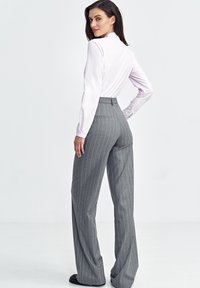 Jasnoróżowa koszula z długim rękawem w połączeniu z szarymi szerokimi spodniami w prążki. Spodnie mają wysoki stan i subtelne tylne kieszenie.