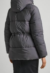 Šedá péřová bunda s kapucí, s prošívaným vzorem, elastickým pasem a strukturovanou tkaninou. Viditelné švy na rukávech a těle.