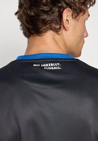 Black sports jersey with a blue collar, featuring white text on the back that reads "MIT HERZBLUT. FUßBALL."