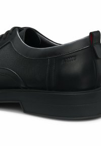 Nahaufnahme eines schwarzen Ledersneakers mit perforiertem Textdetail und strukturierter Gummisohle.