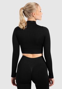 Sort ribbet langærmet crop top med høj hals, parret med højtaljede sorte leggings. Glat tekstur og tætsiddende design.