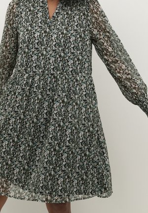 Femme portant une robe noire fleurie à manches longues avec un col en V et une taille froncée.