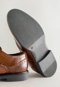 Par de zapatos de vestir de cuero marrón con detalles de brogue, un zapato muestra una suela negra texturizada marcada con el tamaño 42.