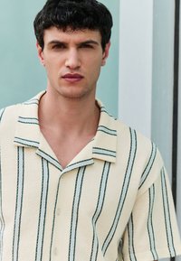 Short-sleeve, light yellow button-up shirt with green vertical stripes, textured fabric, and a notched collar.
