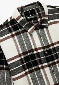 Flanellen shirt in crèmekleurige, zwarte en bruine geruiten patroon. Kenmerkt zich door een puntige kraag, knoopsluiting en een zachte, gestructureerde stof.