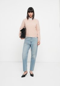 Maglione lavorato a maglia di un rosa chiaro, camicia a scacchi sotto, jeans azzurri a vita bassa, borsa a mano nera piegata e décolleté nere a punta.
