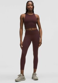 Burgundy sportmelltartó és magasderékú leggings rugalmas anyagból, világosszürke, letisztult dizájnú tornacipővel párosítva.