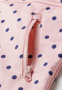 Tissu rose avec des pois bleu marine. Comprend une poche zippée avec une fermeture éclair en plastique et une texture lisse.