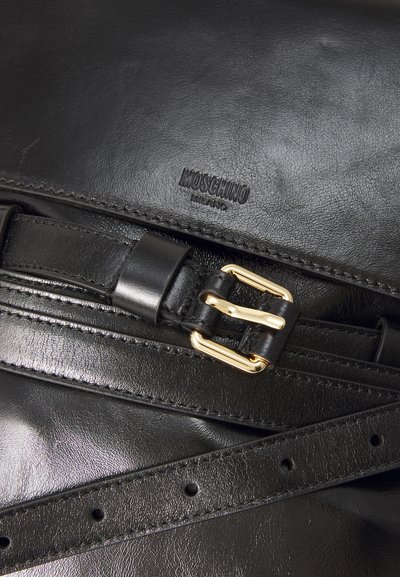 Fekete bőr táska kiemelkedő arany csattal, Moschino logóval és texturált felülettel, állítható pánttal és varrási részletekkel.